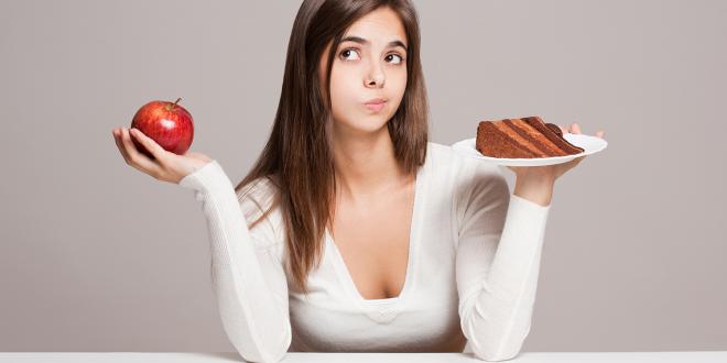 a young woman choosing between an apple and a slice of cake