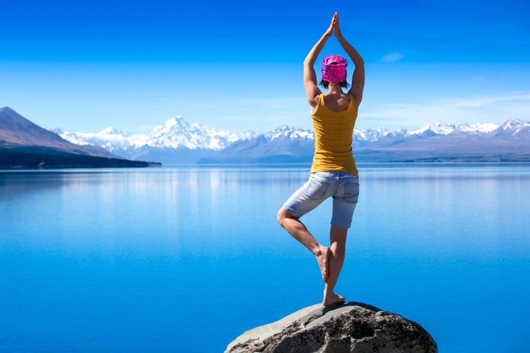 A young woman doing a yoga pose for balance on a rock overlooking a lake.